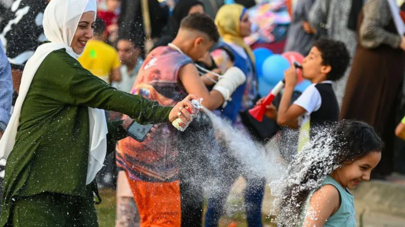 Getty Images A woman playfully sprays a girl with foam as they celebrate Eid